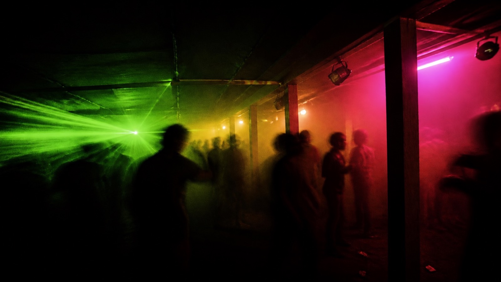 Blurred silhouettes dancing in a basement club under green and magenta light
